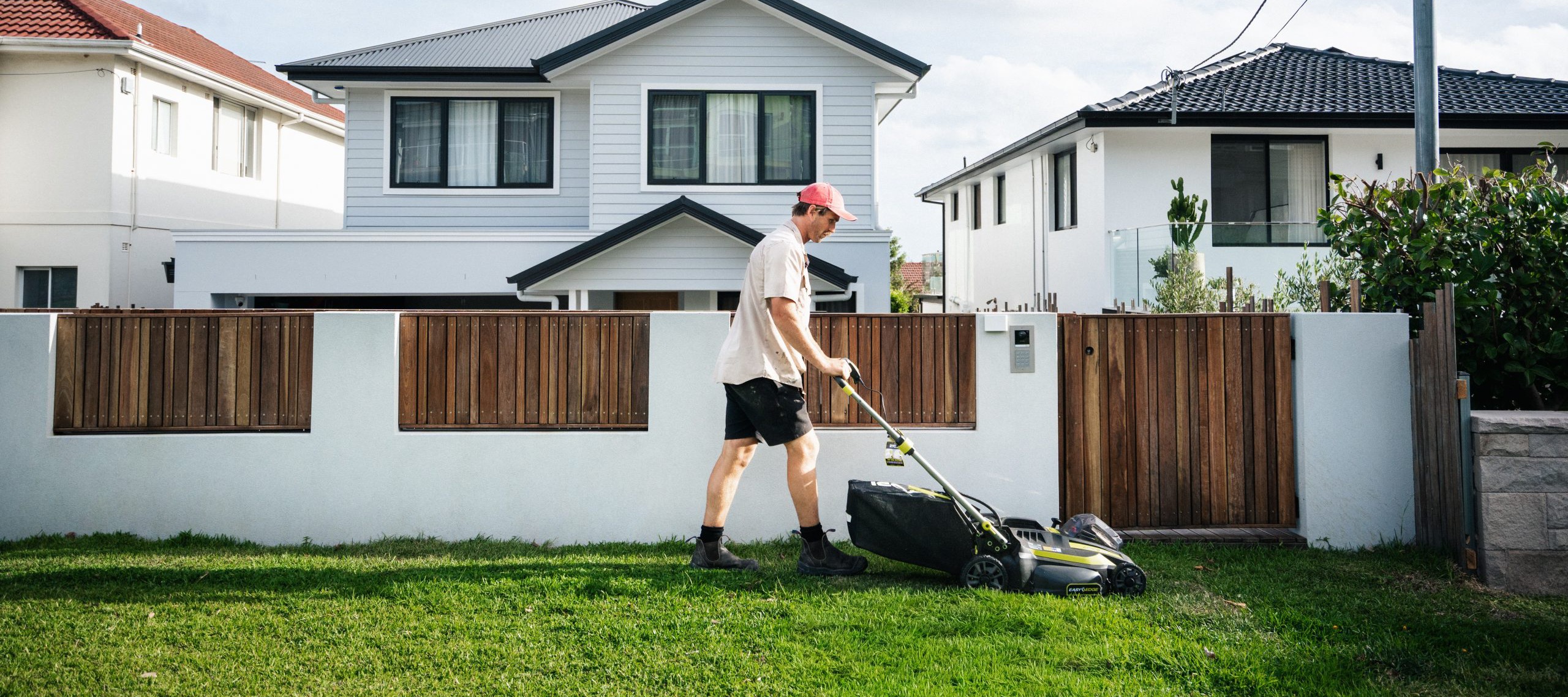 Landscaper mowing a lush green lawn in front of a landscaped home in the Northern Beaches